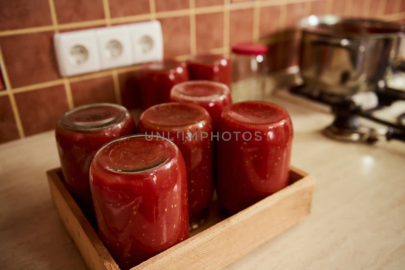 Still life with sterilized tins of freshly brewed tomato sauce, passata or juice, upside down on a wooden crate. Canning organic homegrown vegetables for the winter. Making preserves. Conservation