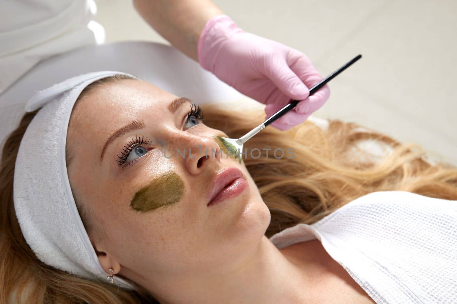 Cosmetologist applying a clay mask to the face of beautiful woman. Spa treatment in the beauty salon