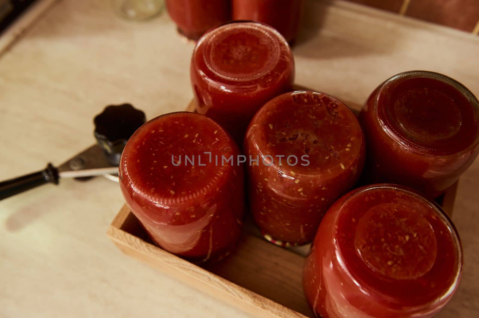 Still life. Sterilized tins of tomato sauce or juice upside down on wooden crate next to a seaming key on kitchen countertop. Cooking passata according to a traditional recipe. Canning for the winter