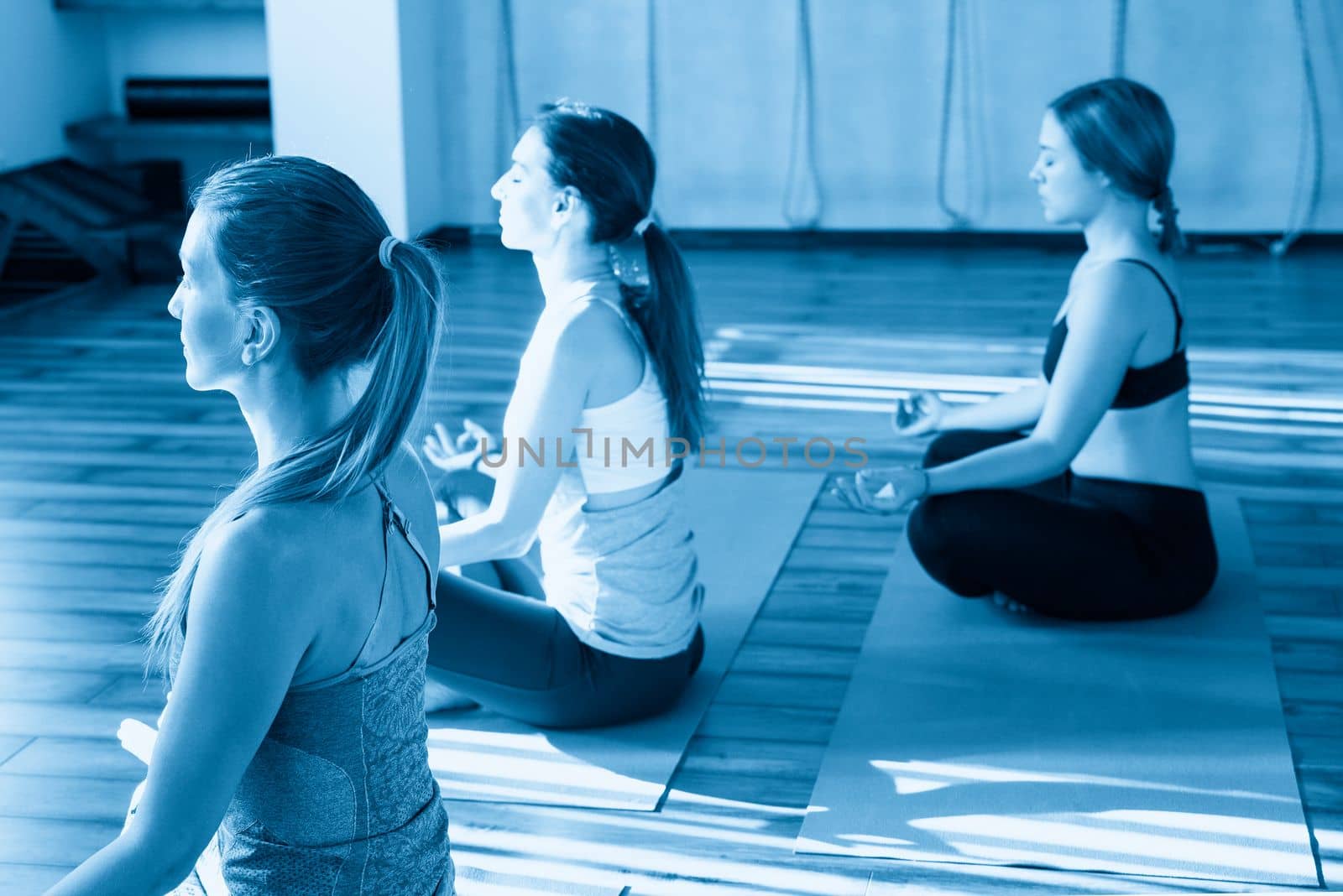 young women in yoga class sitting and relaxing making meditation lotus pose by Mariakray