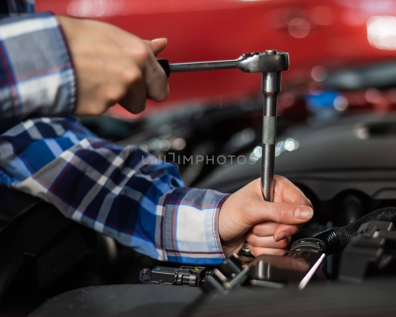 Female auto mechanic unscrewing a nut to replace a car spark plug. by mrwed54