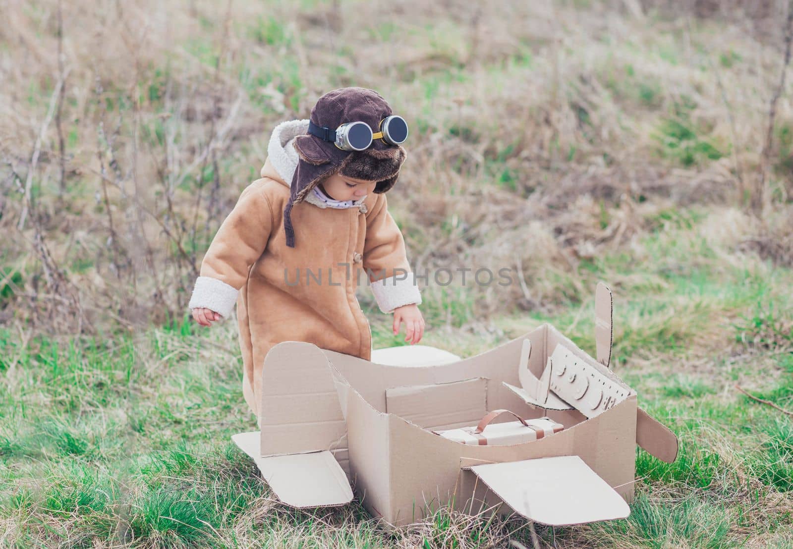 Charming baby in aviator's clothes gets on the cardboard plane.