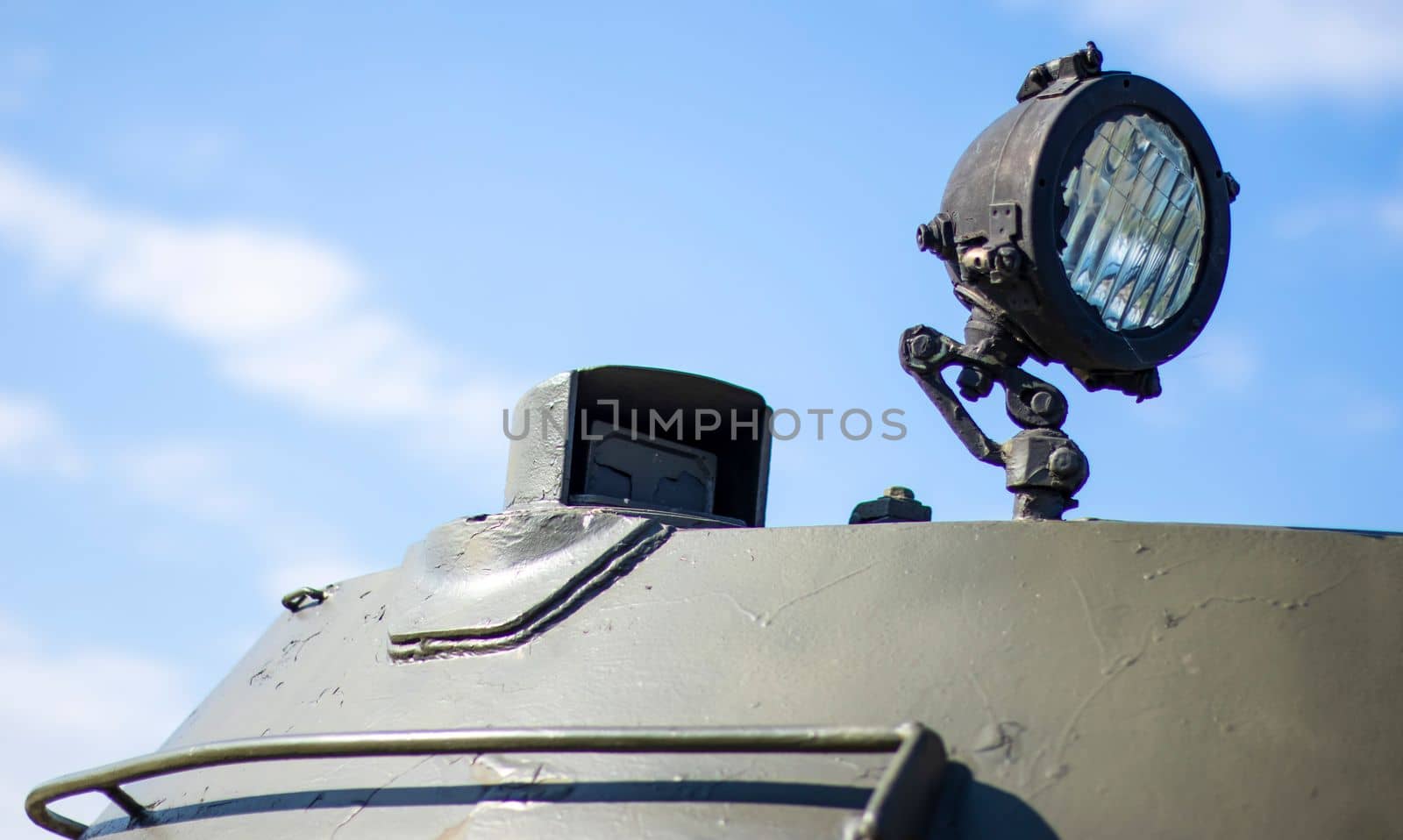 Front headlight of a Soviet battle tank. Very bright searchlight on the tank turret, close-up. Armored infantry fighting vehicle. Fragment of an old armored personnel carrier, khaki headlight