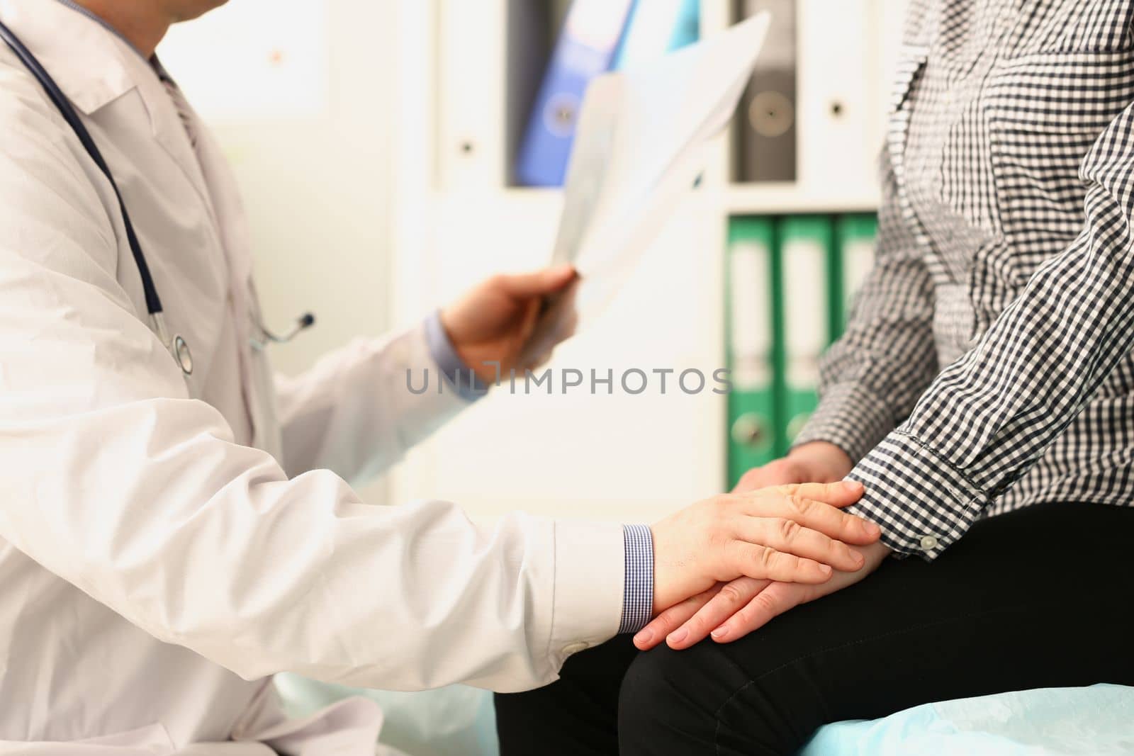 Doctor examines x-ray and holds patient hand. Medical services and psychological help concept