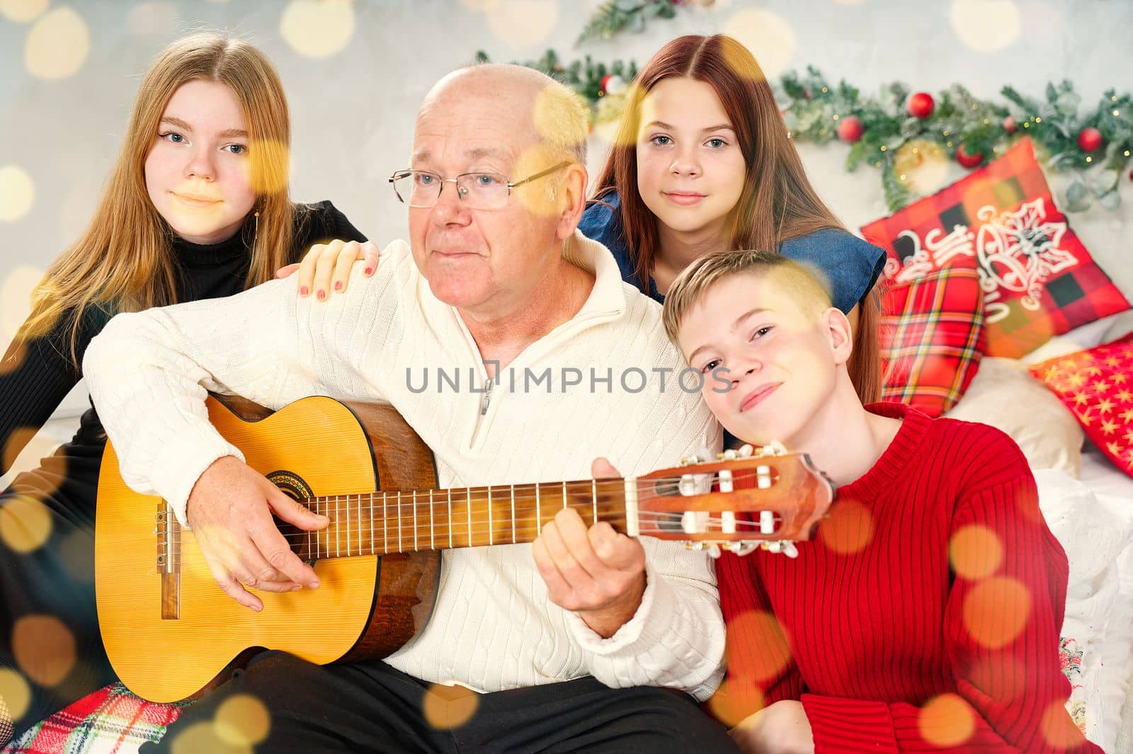 Grandfather playing guitar during christmas for grandchildren. Happy man 60s playing guitar christmas songs. Happy christmas atmosphere.