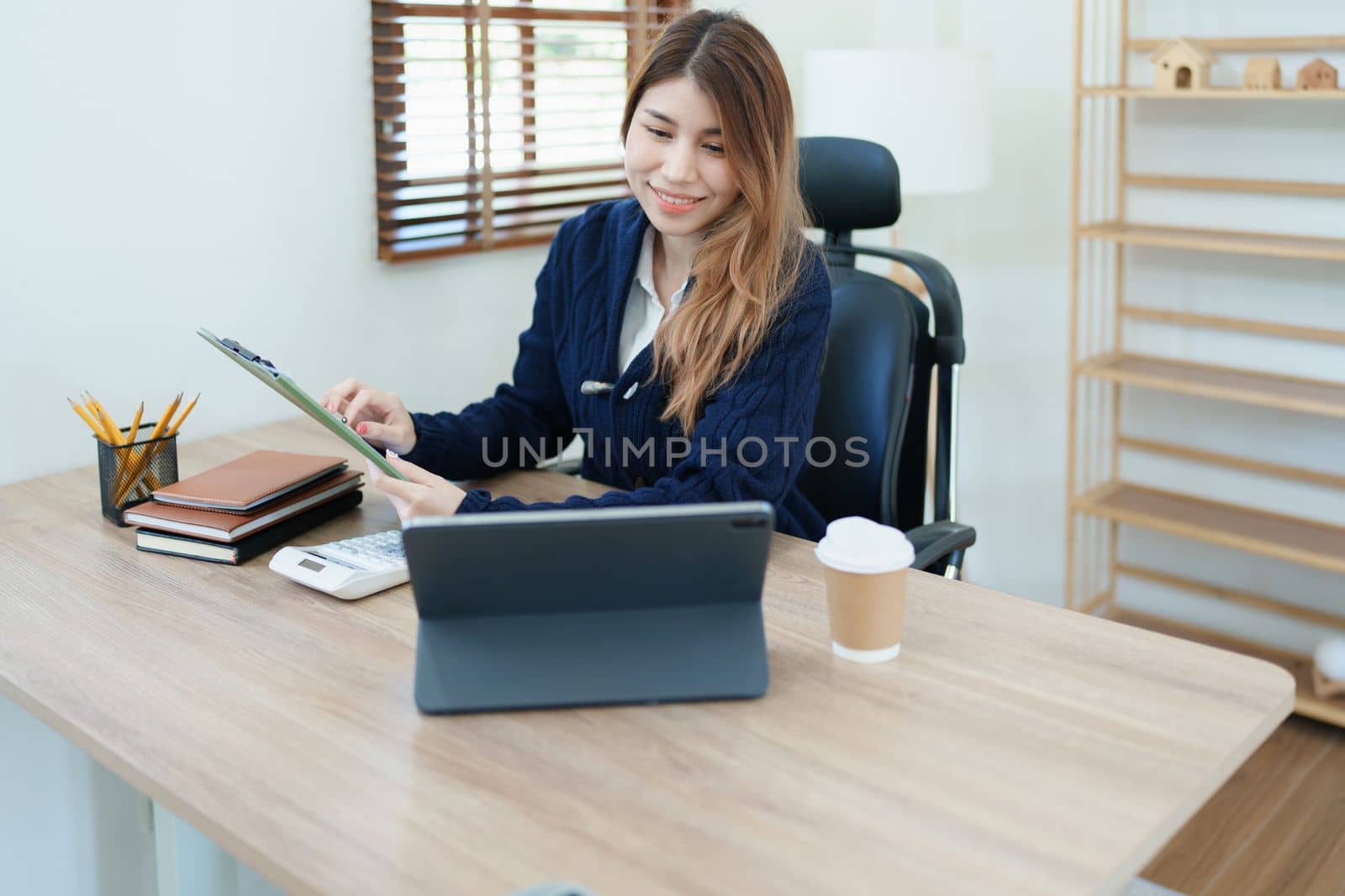 Portrait of a thoughtful Asian businesswoman looking at financial statements and making marketing plans using a computer on her desk.