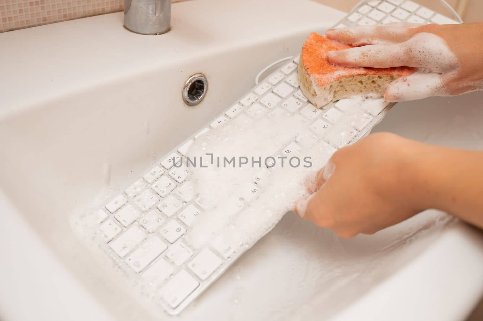 Woman washing white computer keyboard with a sponge with foam