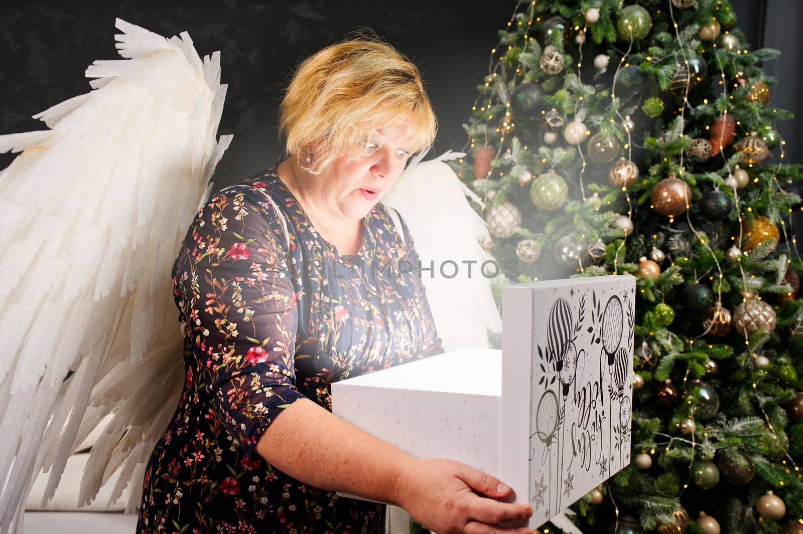 smiling lonely woman opens a christmas present near the christmas tree. Christmas wonder. by PhotoTime