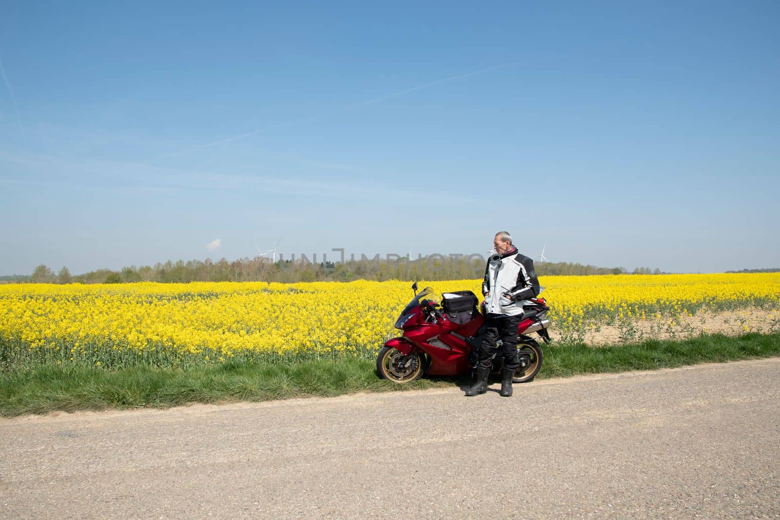 biker with red motorcycle stands by the roadside next of a blooming yellow field of rapeseed travel in nature in early spring. High quality photo