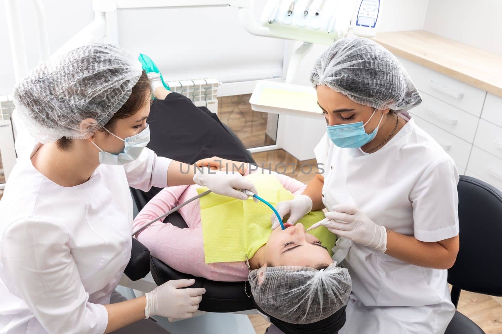 Dentist and assistant performing dental treatment inmodern dental clinic, patient laying in a chair by Mariakray