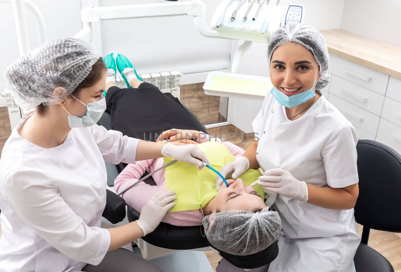 Dentist and assistant performing dental treatment inmodern dental clinic, patient laying in a chair by Mariakray