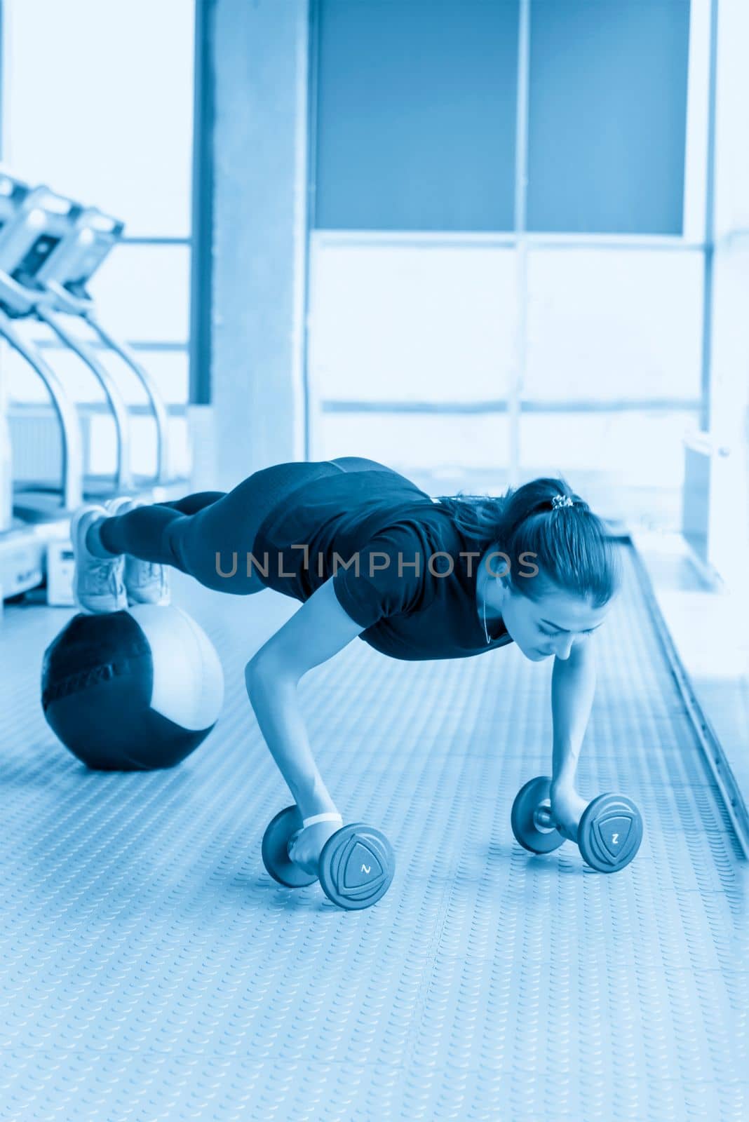 Woman doing floor workout at gym. Fitness girl doing dumbbells and medicine ball plank by Mariakray