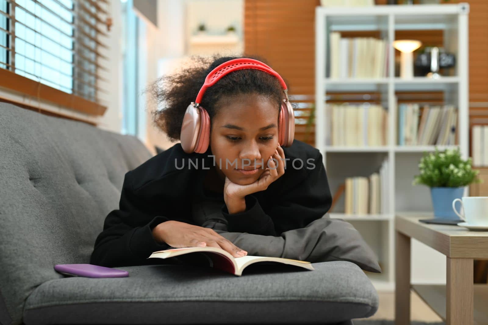 Teenage woman lying on couch and reading favorite literature. People and leisure activity concept.