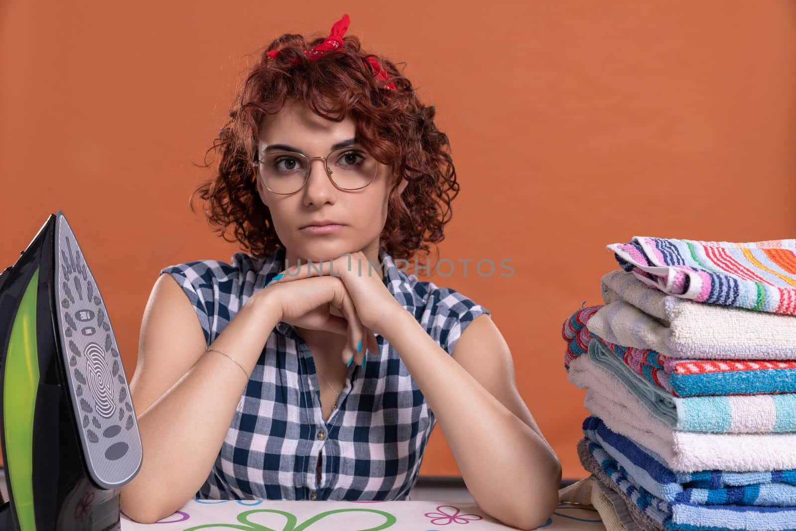The girl, having finished her work, waits for the next one. The ironed towels lie on the ironing board. Isolated from the background.
