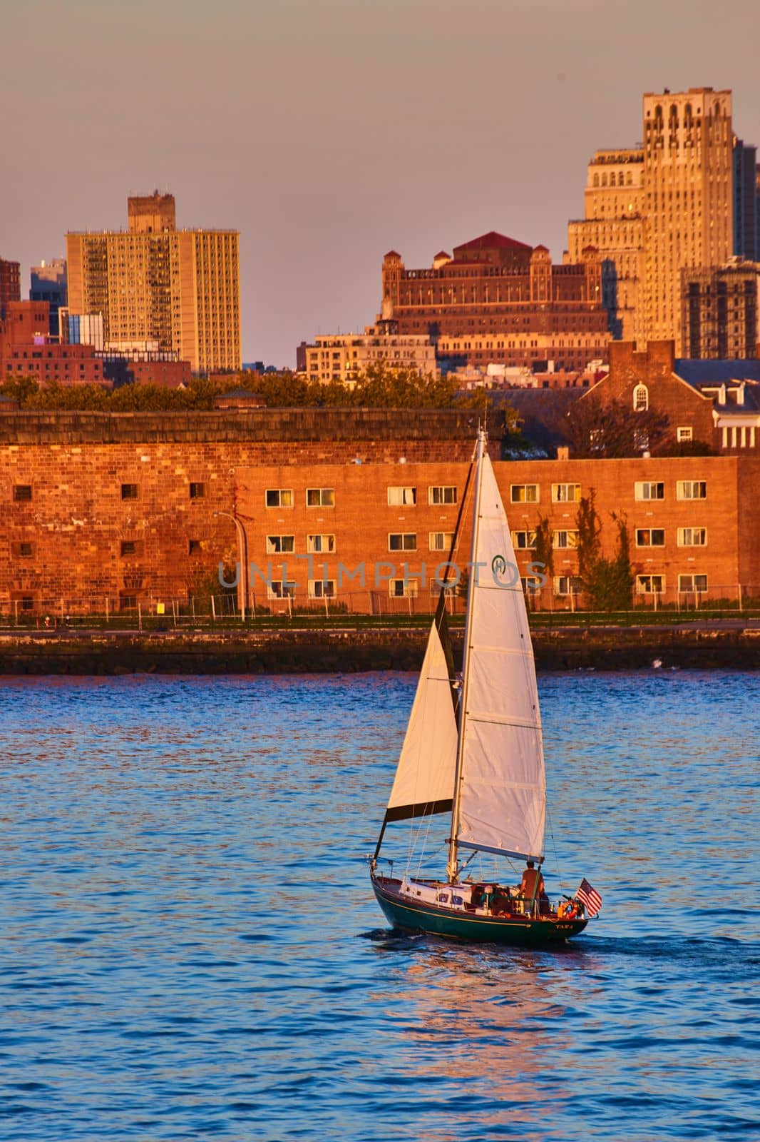 Image of Dusk golden hour focus on sailboat in waters by Governors Island in New York City