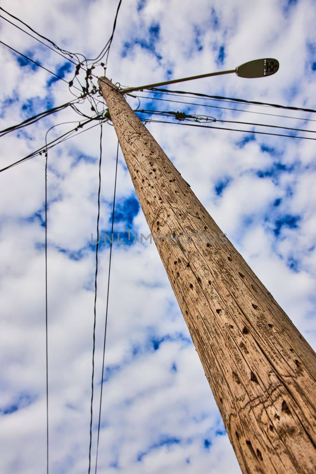 Detail looking up textured wood telephone pole with spotty clouds on blue sky by njproductions