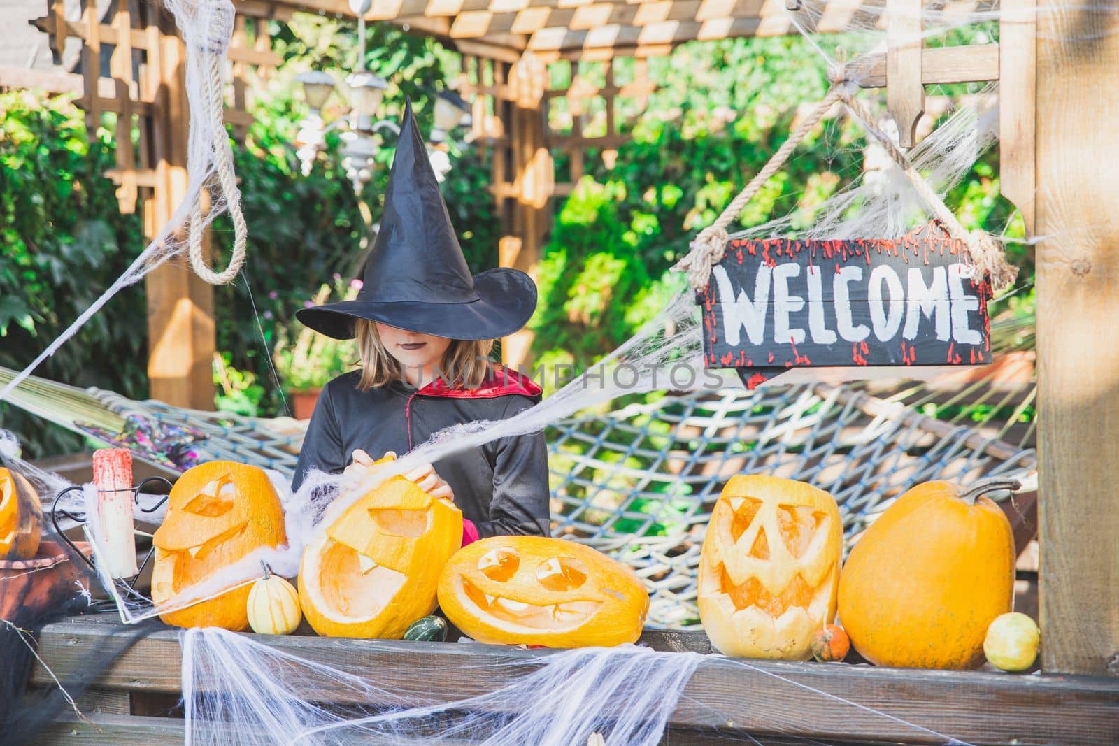 girl in a mantle and a hat stands near the Halloween pumpkins.