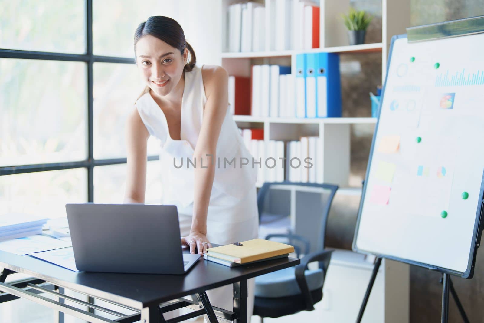 Portrait of a woman business owner showing a happy smiling face as he has successfully invested her business using computers and financial budget documents at work by Manastrong