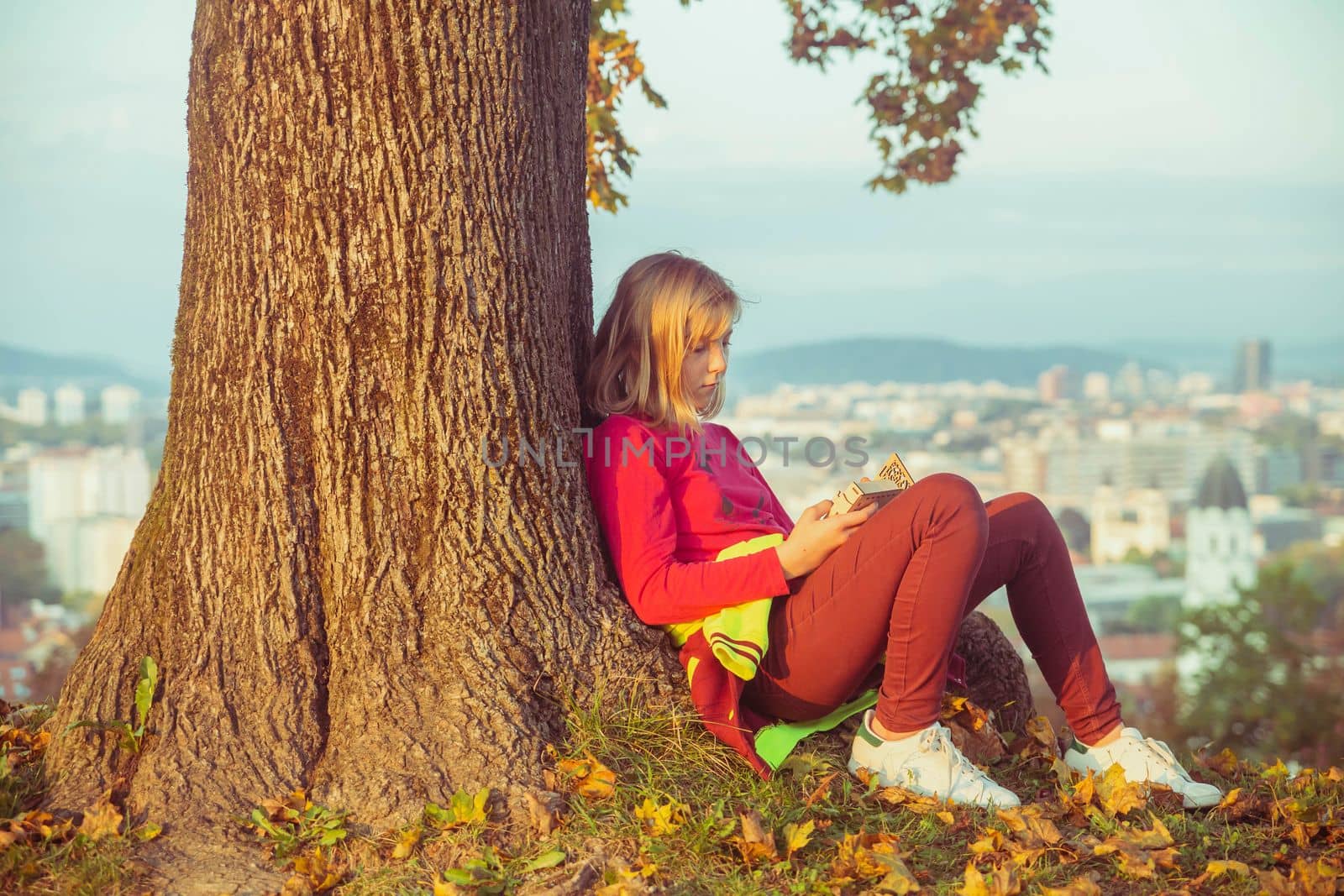 teenage girl sitting under an autumn tree on a hill on the Sunset.