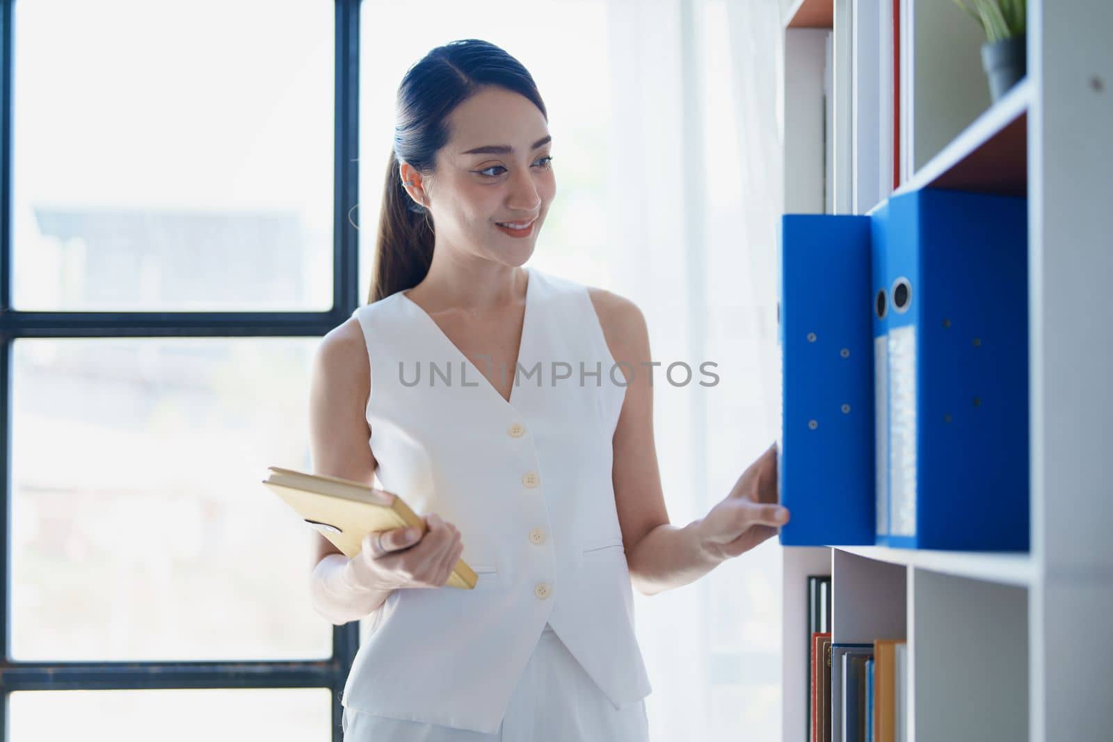 portrait of Asian female employees notebooks and pick up important documents to start their morning work. by Manastrong