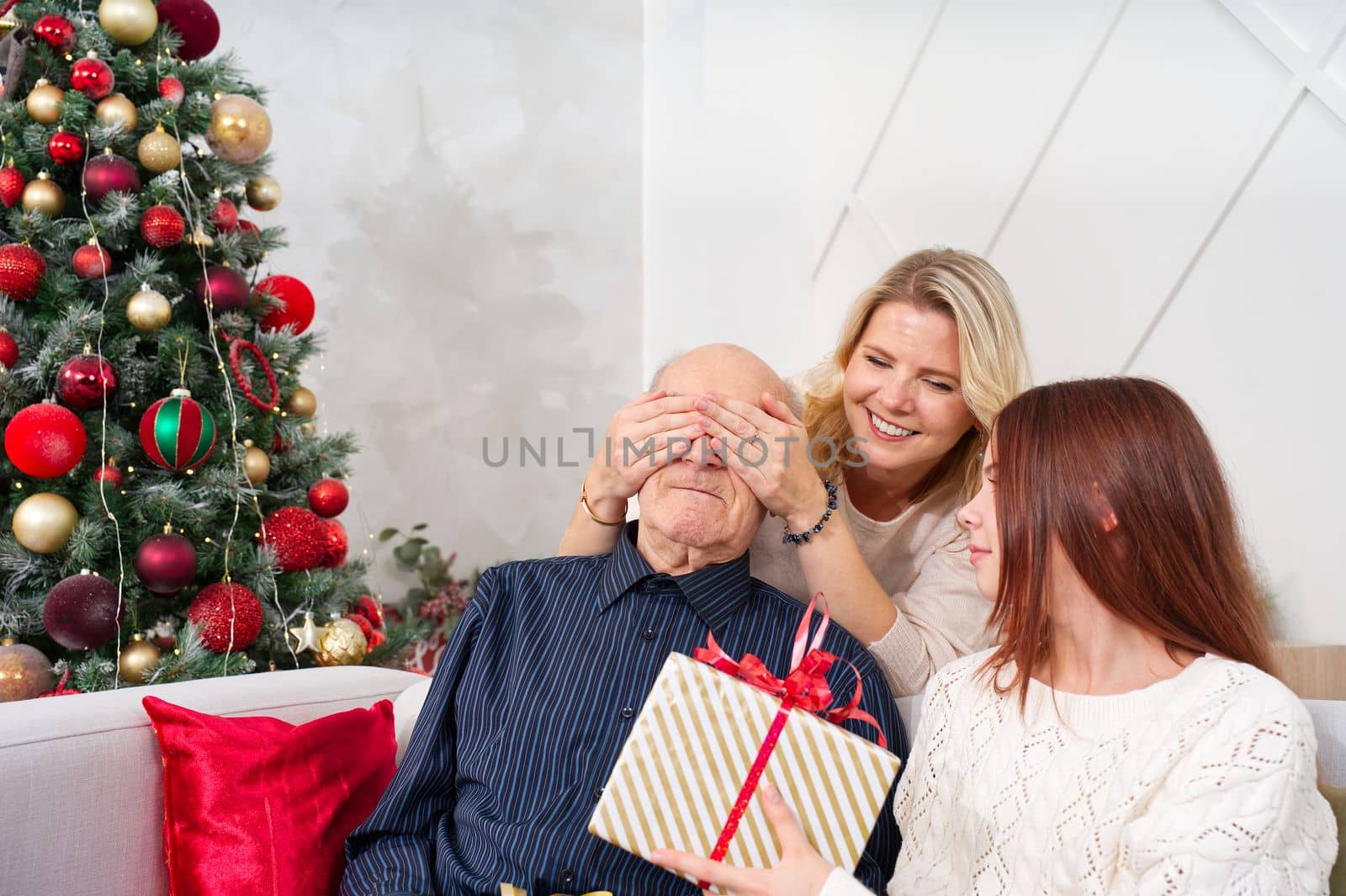 Granddaughters give a gift to grandfather. Happy senior man embracing his granddaughter while receiving a gift on Christmas at home. Happy family grandfather with cute excited granddaughter.