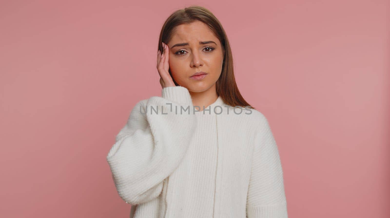 Hipster young adult woman in sweater rubbing temples to cure headache problem, suffering from tension, migaine, stress, grimacing in pain, high blood pressure isolated alone on pink wall background
