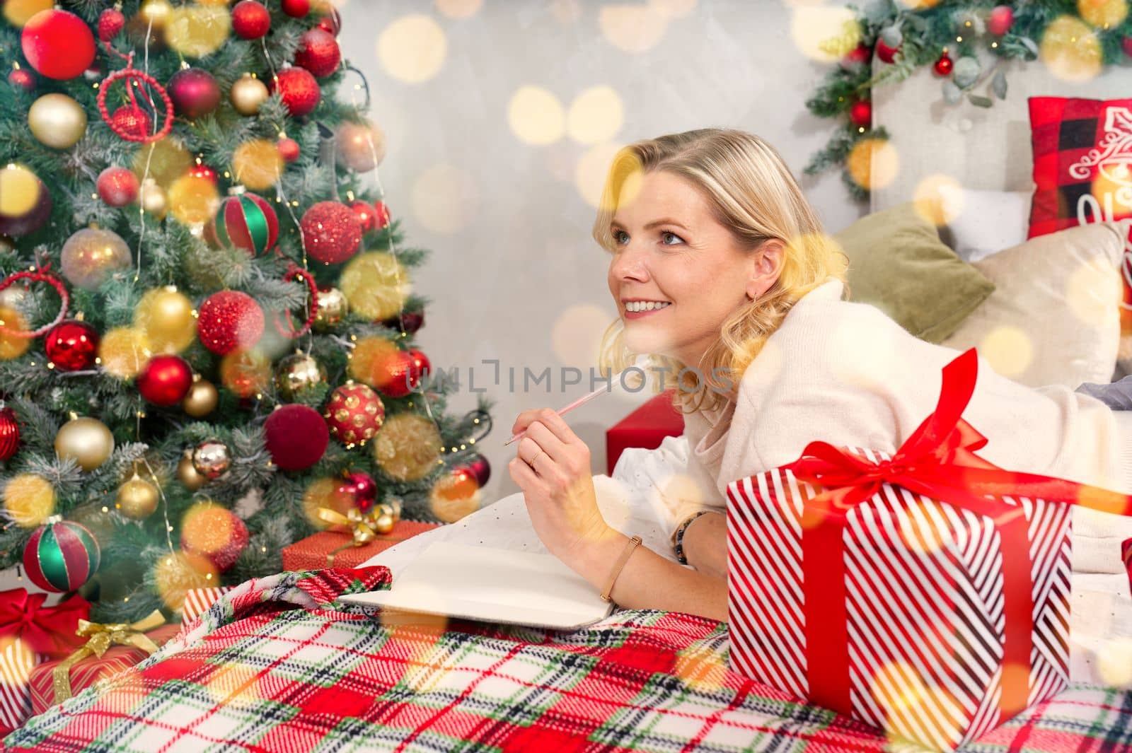happy woman with pen and notebook making wish list or to do list for new year in bed over christmas tree. xmas holidays concept by PhotoTime