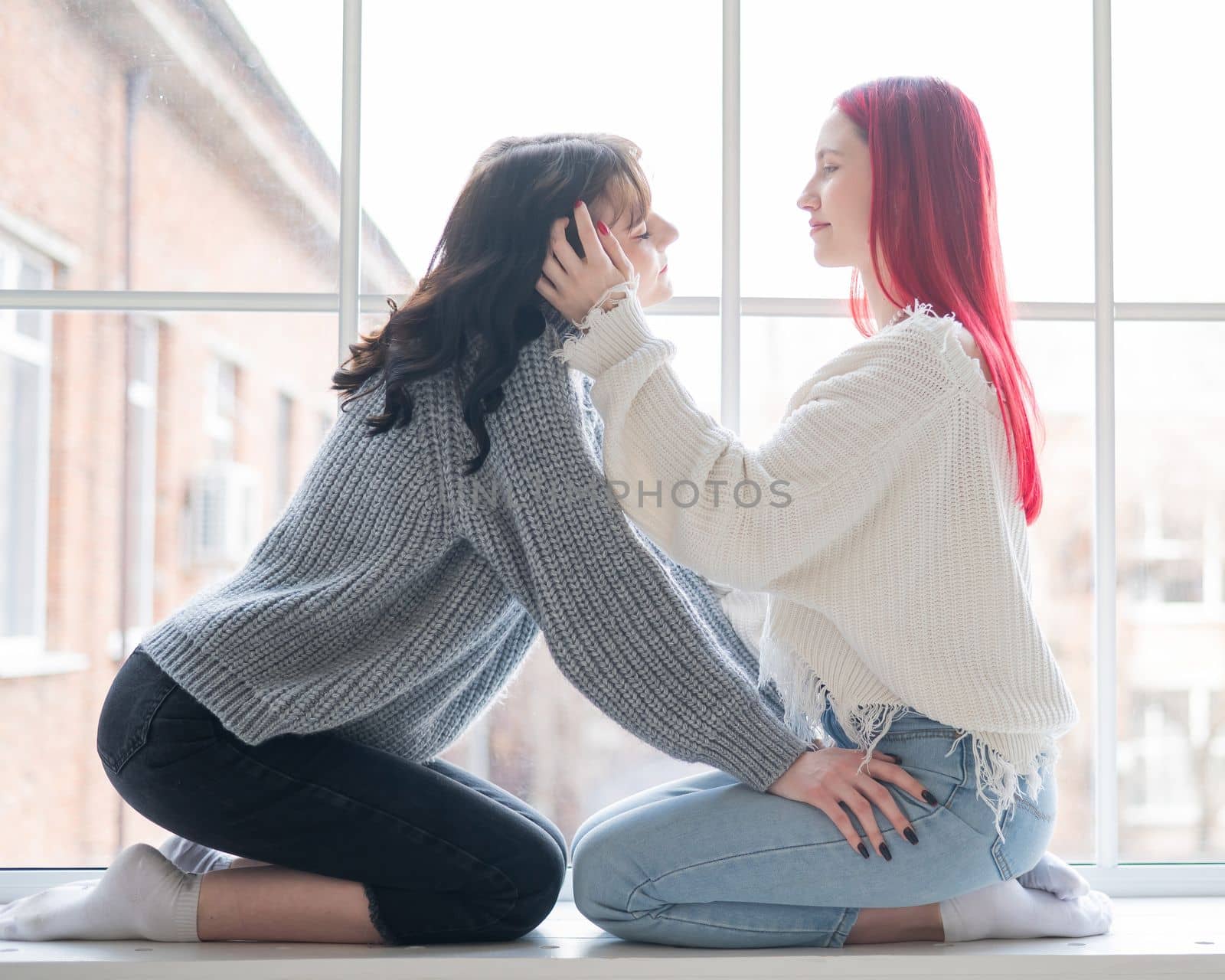 Two women dressed in sweaters sit by the window and gently hug. Lesbian intimacy