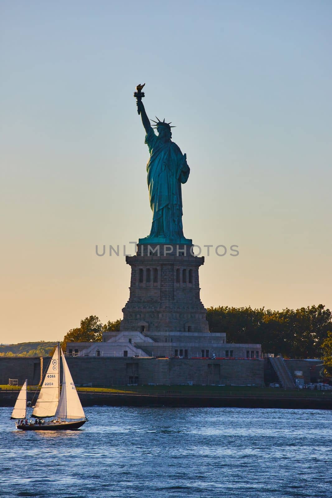 Image of Small sailboat sails past Silhouette of Statue of Liberty in New York City during sunset soft light