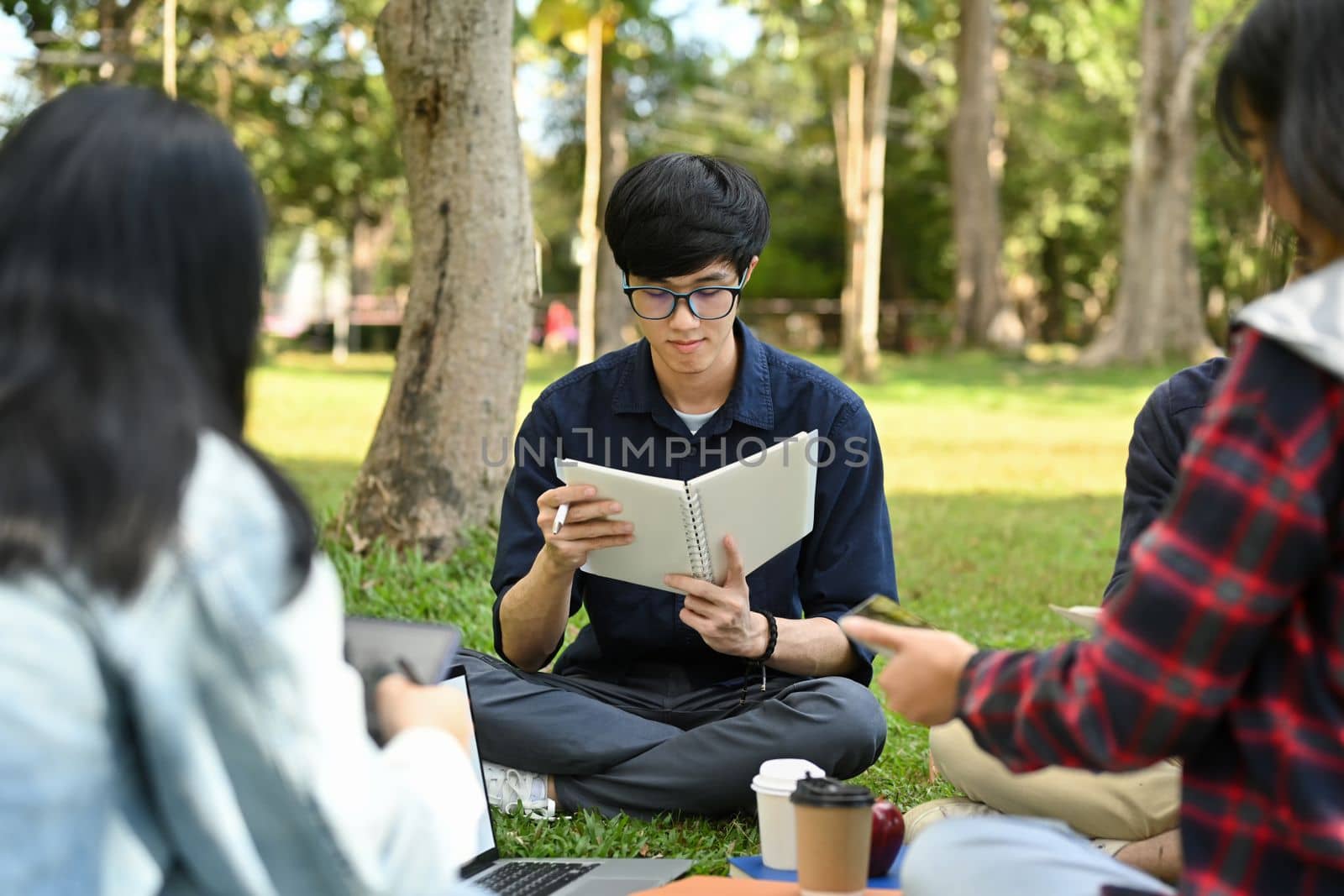 Asian student man reading books, preparing for exam while sitting in the campus with friends. Education and lifestyle concept.