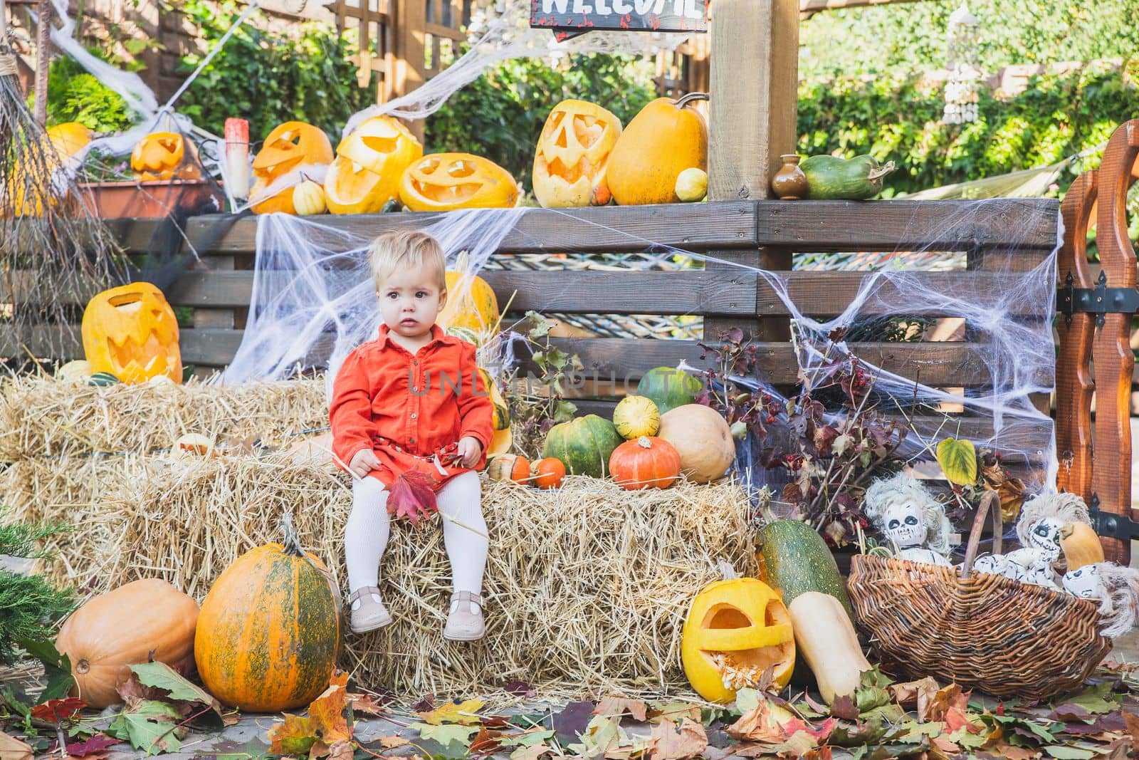 baby sitting on a haystack surrounded by halloween pumpkins.
