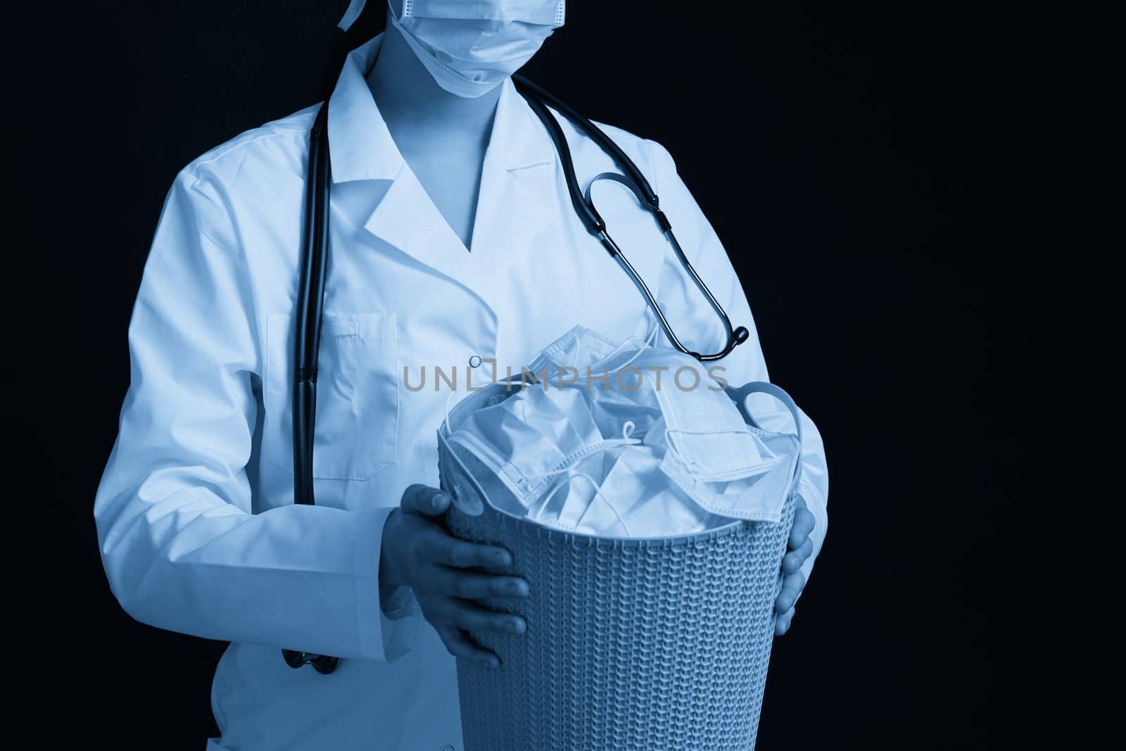 Doctor holding bucket full of used facial masks, throwing them away as symbol of epidemic ending by Mariakray