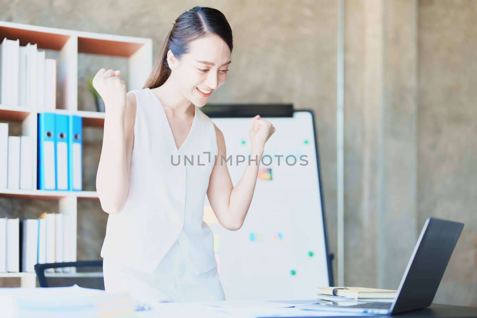 Portrait of a woman business owner showing a happy smiling face as he has successfully invested her business using computers and financial budget documents at work by Manastrong