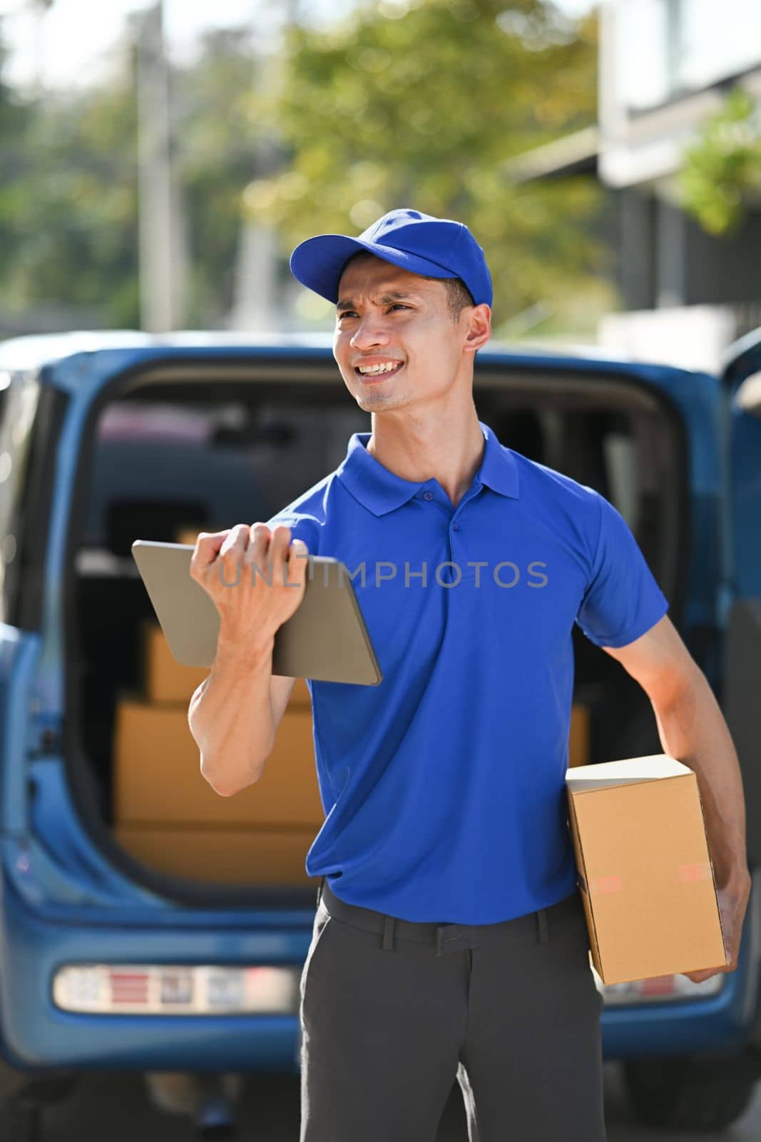 Portrait of delivery man carrying cardboard parcel and using digital tablet. Delivery service, post and shipping concept by prathanchorruangsak