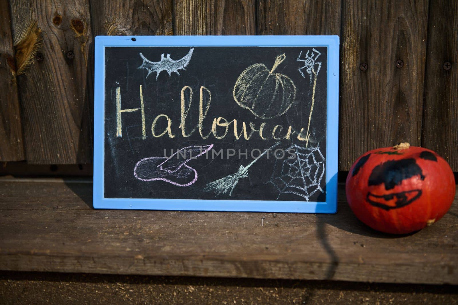 A blackboard with lettering Halloween and small pumpkin on the wooden doorstep by artgf