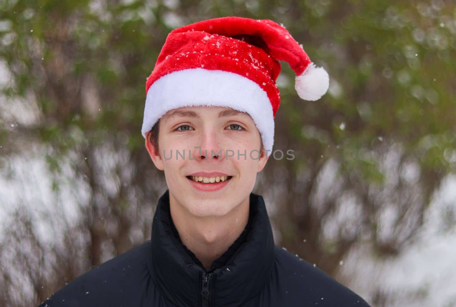 Close-up portrait of a 14-17 year old weighty boy wearing a Santa hat in snowy weather.