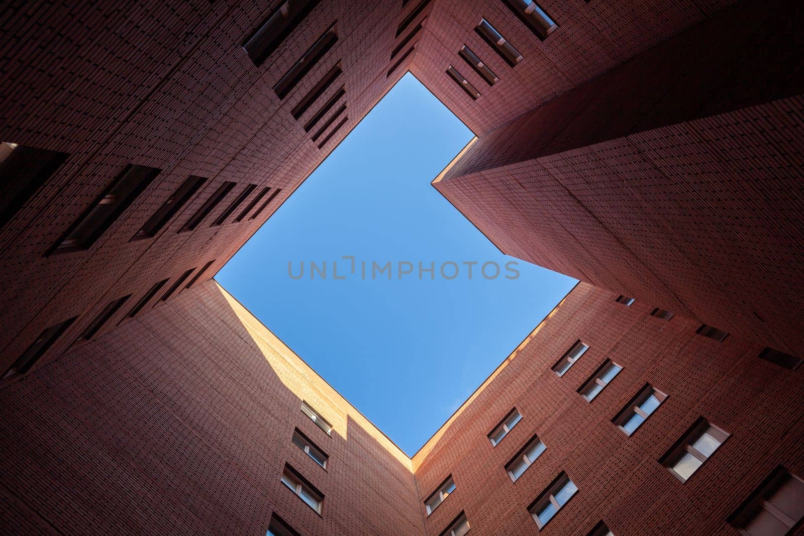 Brick high-rise new square house on a blue sky background. View from the courtyard to the top of the sky. Luxury housing and offices for work.