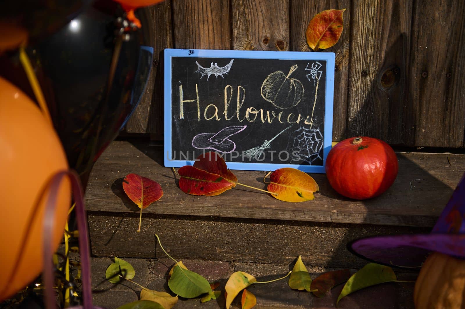 Close-up of a chalkboard with lettering Halloween, a pumpkin on the wooden doorstep with dry autumn fallen leaves