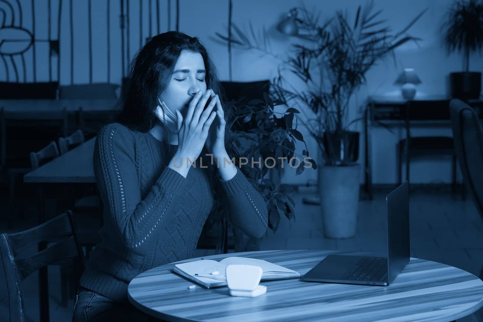 sick young woman with pills and thermometer on a table working on a laptop from home on quarantine isolation. Online work, stay home concept