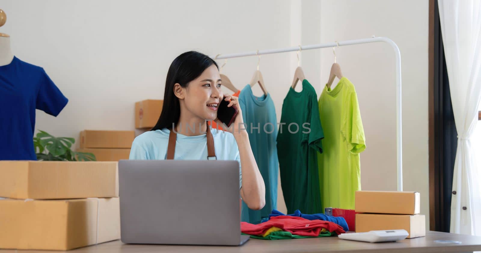 Beautiful asian woman online seller confirming orders from customer on the phone, Start small businesses SME owners female entrepreneurs use a laptop at home,pack and delivery situation concept..