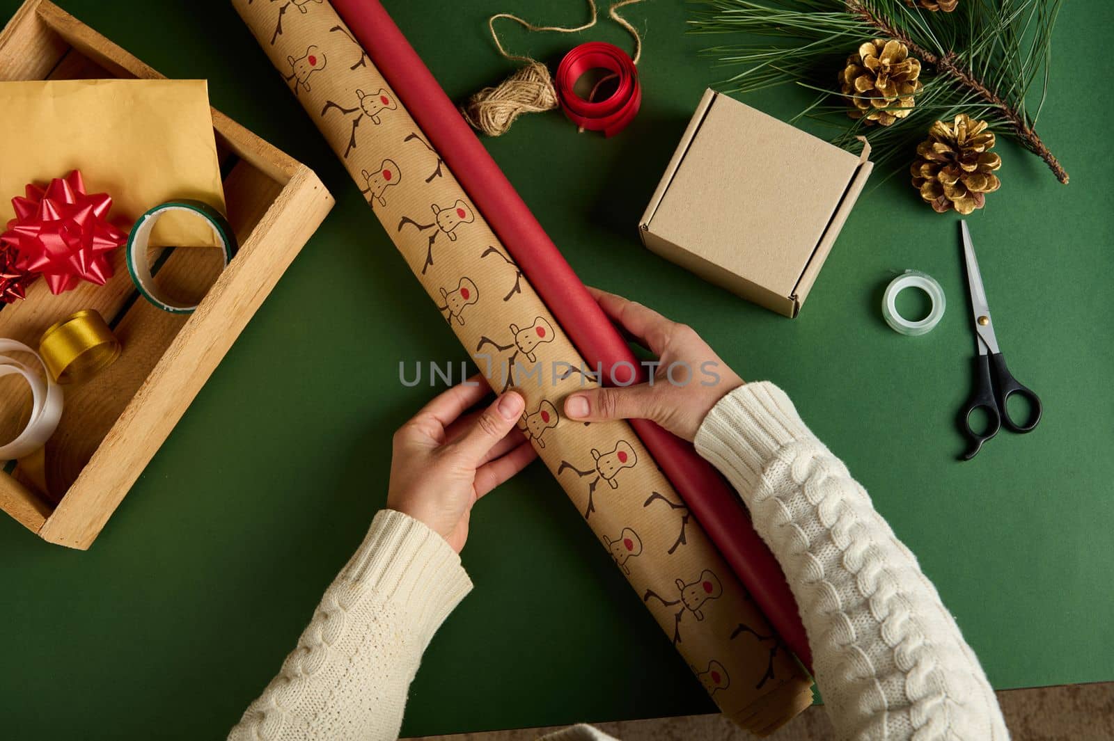 Top view hands hold wrapping paper over a green background with decorative materials for diy presents. New Year and Christmas preparations. Handwork art. Craft. Packing gifts. Boxing Day. Magic mood