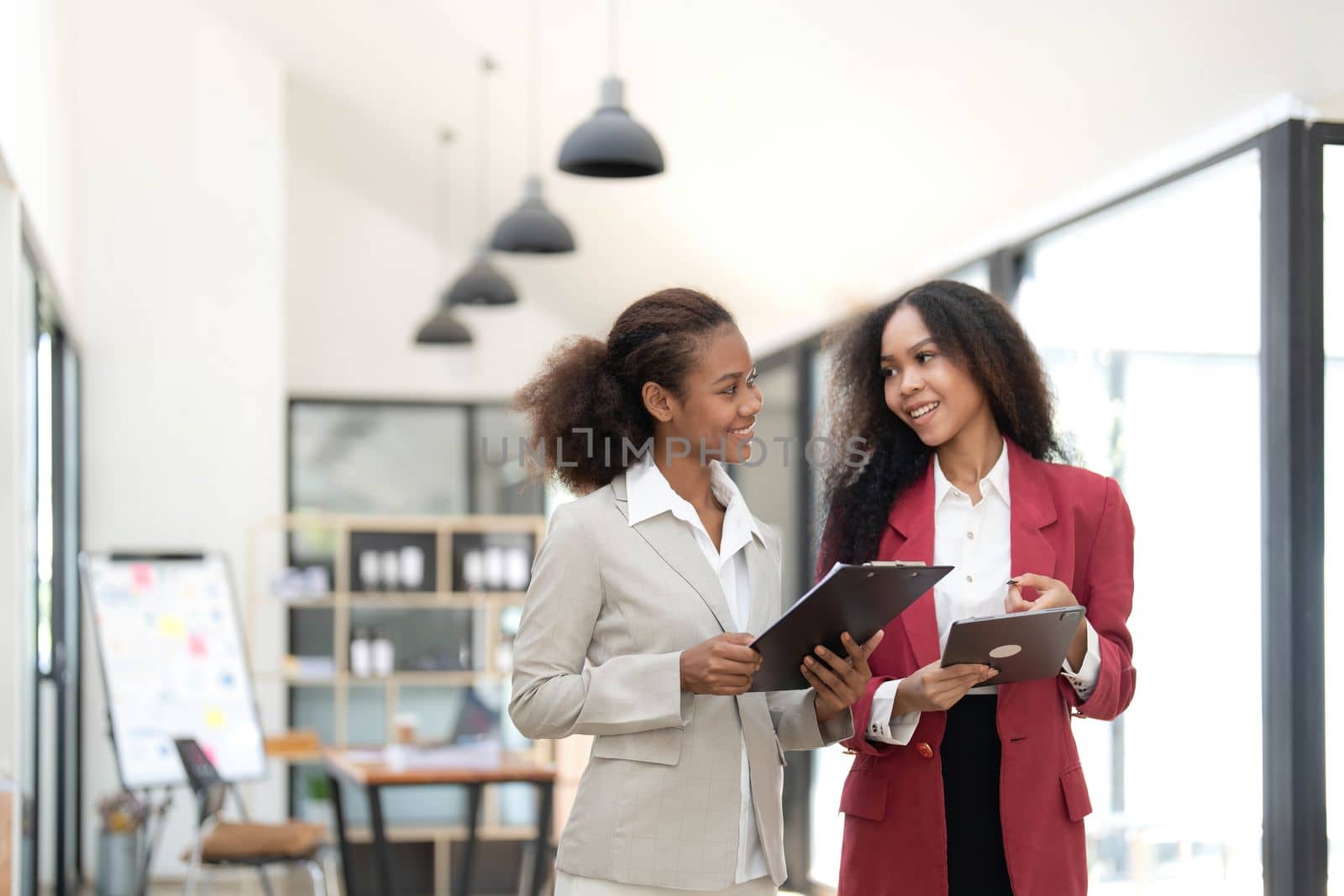 Smiling diverse colleagues businesswomen working on laptop together, looking at screen, stand at desk in office, employees discussing project strategy, sharing ideas.