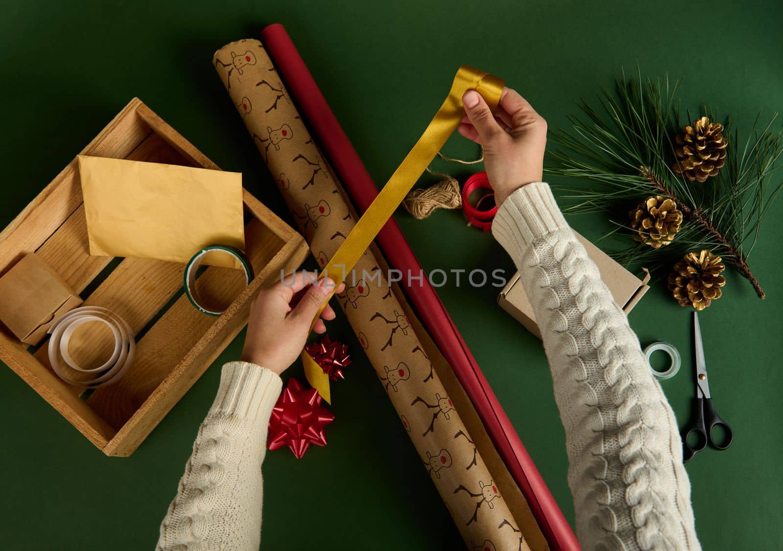 Top view hands hold a golden tape over wrapping materials. Packing Christmas and New Year gifts. Boxing day. Happy holiday present, surprise. Magic time. Celebration winter event. Handwork art craft