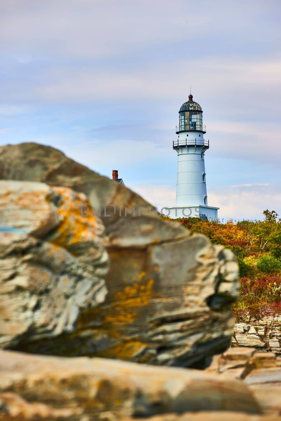 Image of Looking over large rocks with lighthouse in the background and fall forest