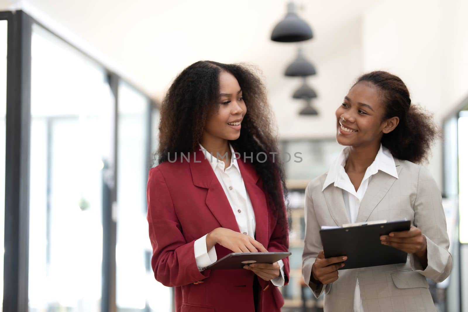 Smiling diverse colleagues businesswomen working on laptop together, looking at screen, stand at desk in office, employees discussing project strategy, sharing ideas.