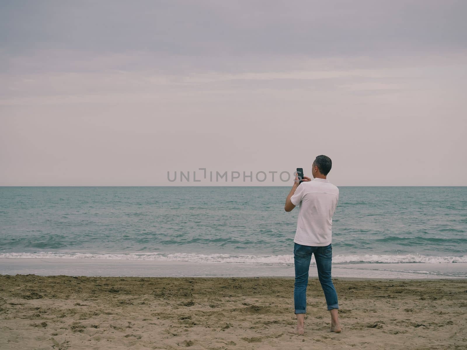 Young man taking picture photo of beach sunset holding a smartphone