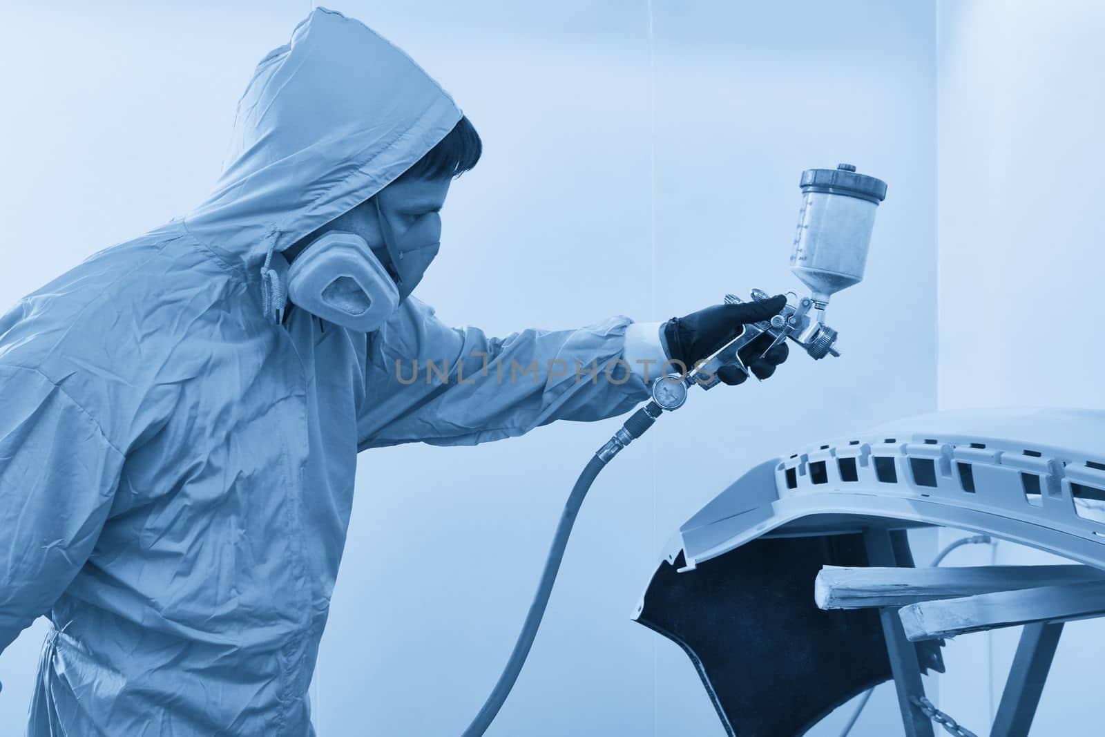 Mechanic painting bumper of a car with sprayer in painting booth