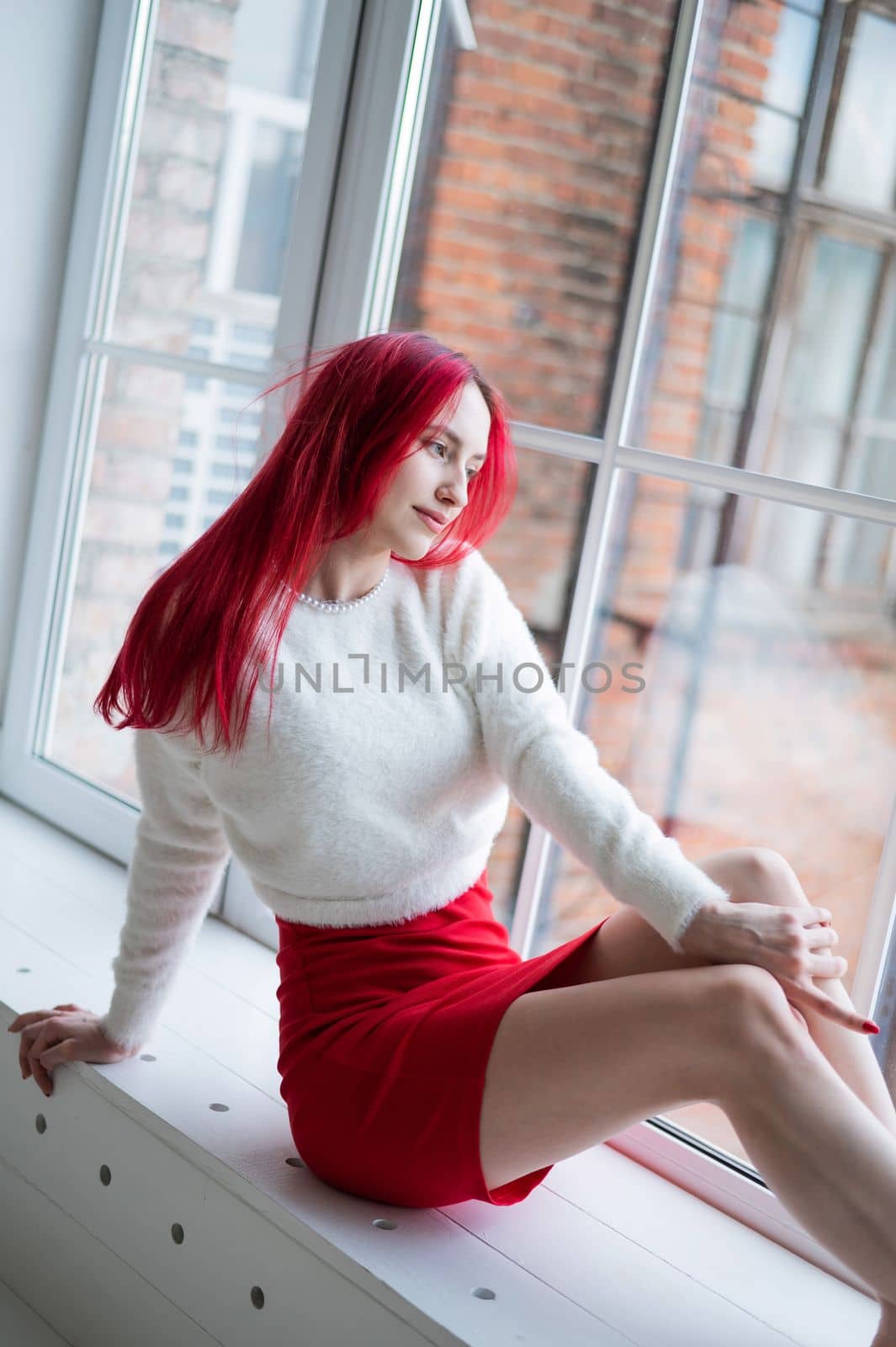 Caucasian woman with red hair sitting on the windowsill. by mrwed54