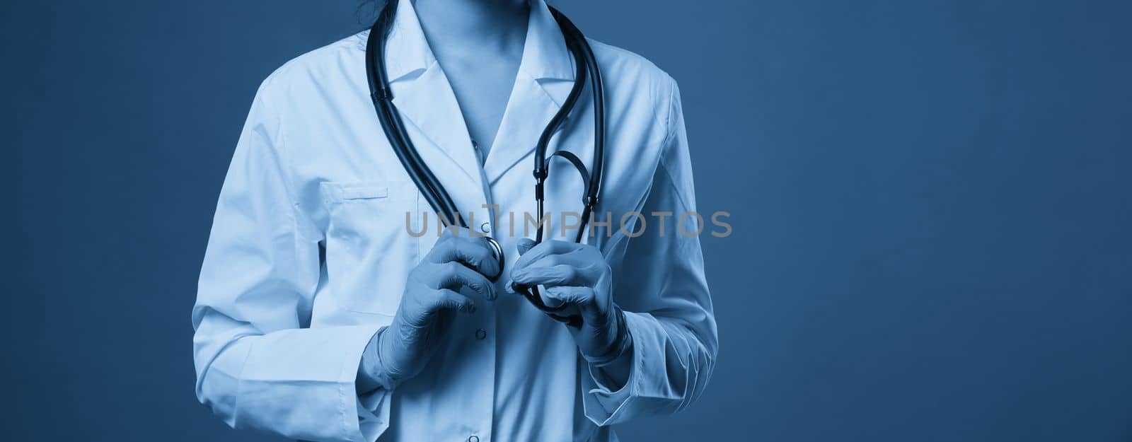 Young doctor with stethoscope against dark blue background, studio shot with copy space by Mariakray