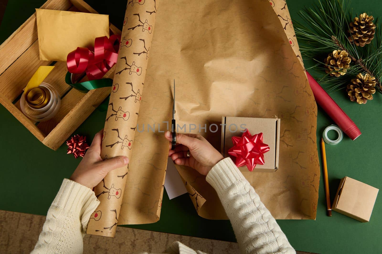 Top view woman in warm beige sweater, cutting wrapping paper with deer pattern for packing gift for Christmas, New Year by artgf